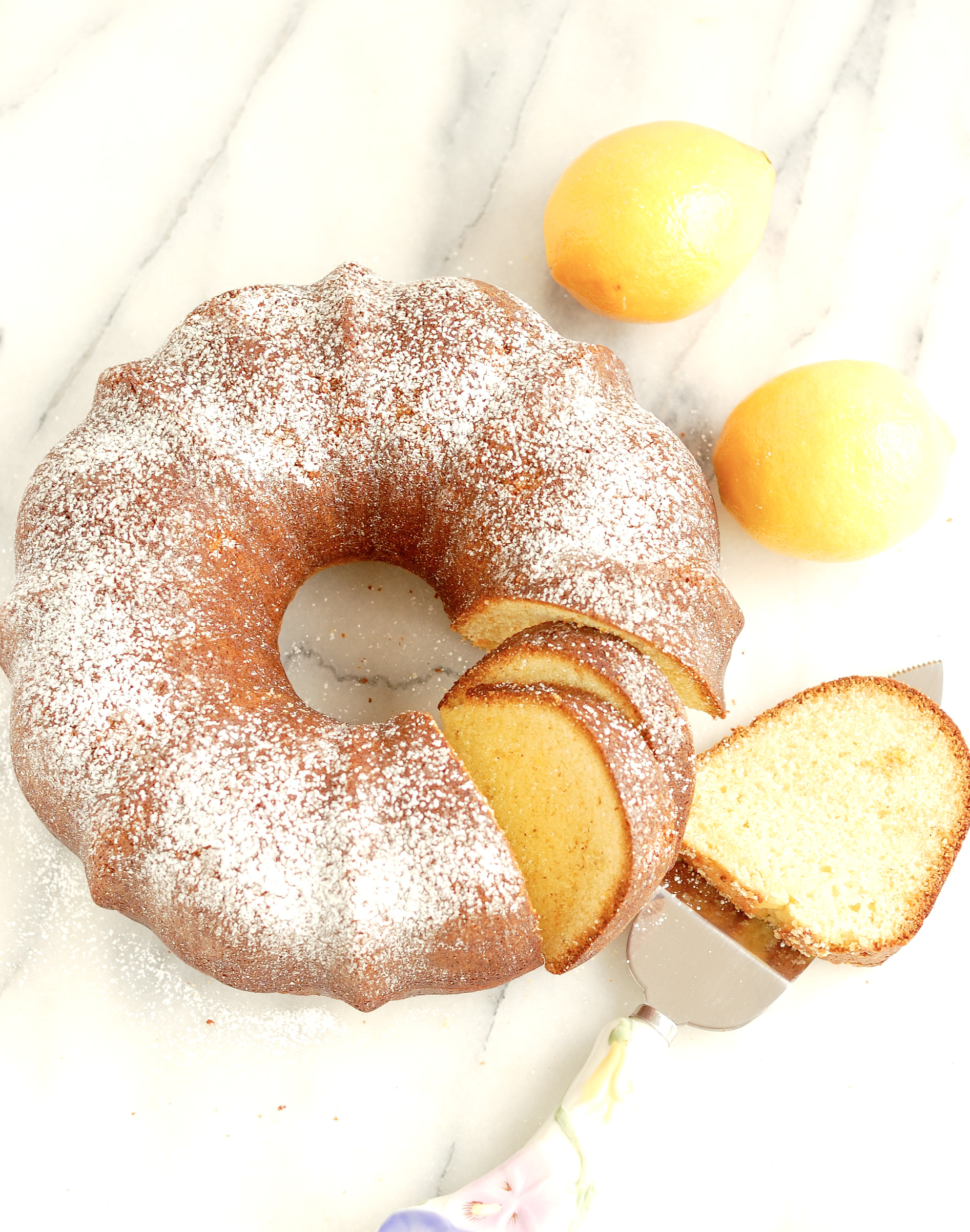 a slice cake and some lemons on a marble table.