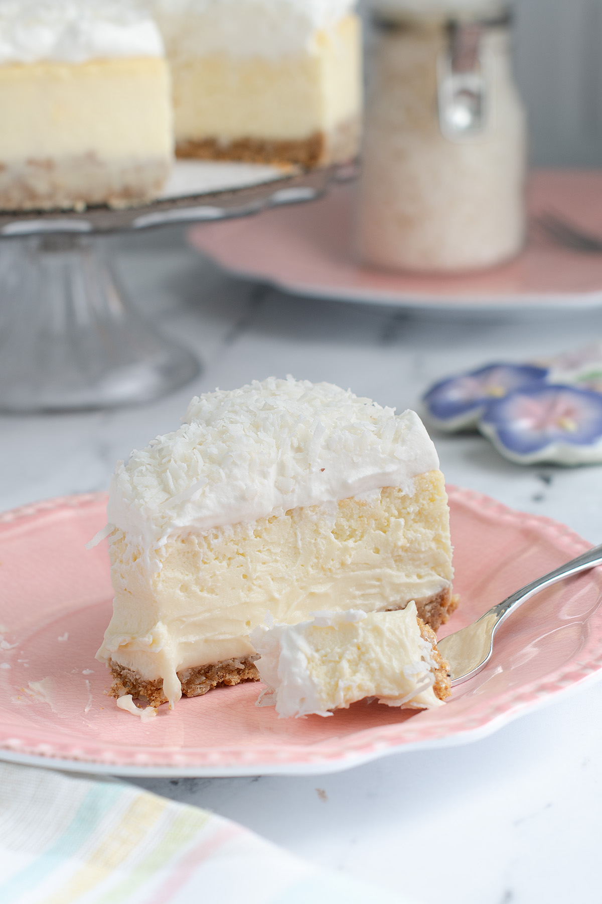 a slice of coconut cheesecake and a fork on a pink plate.