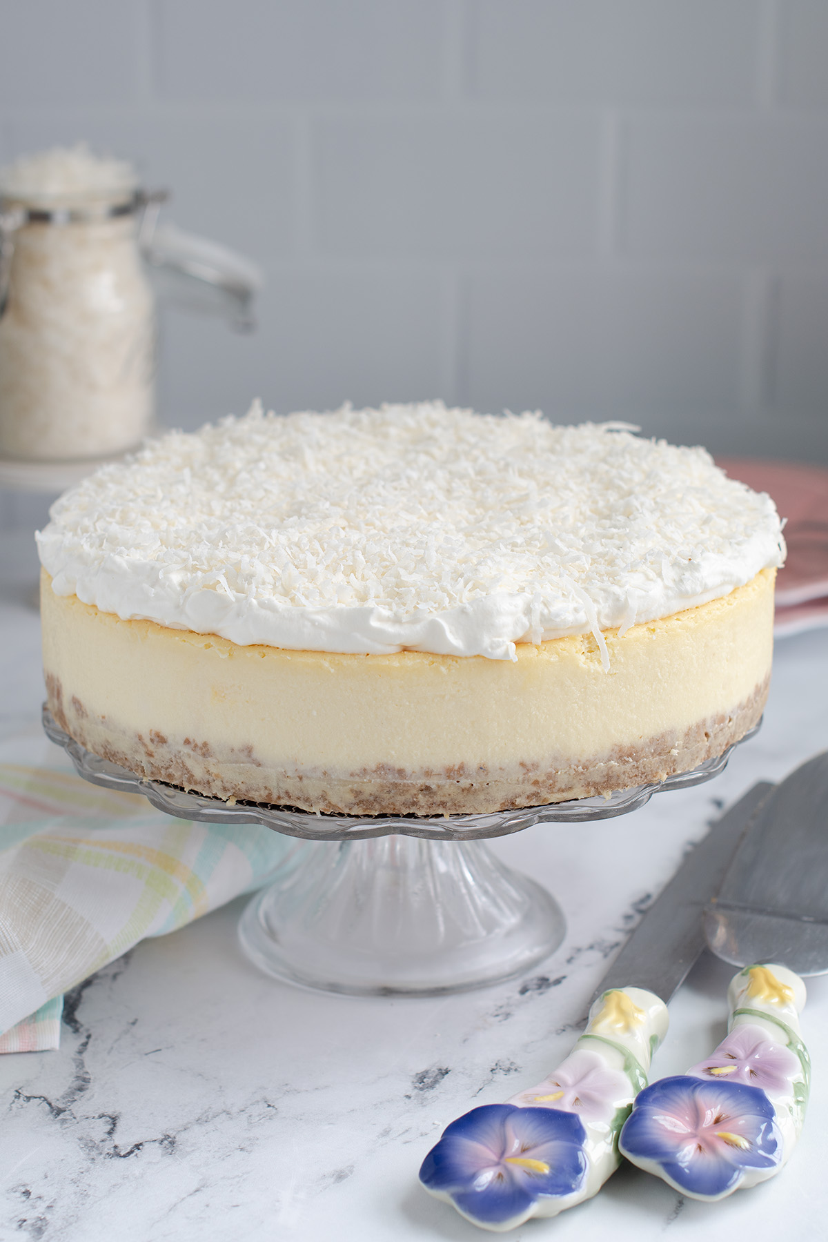 a coconut cheesecake on a glass cake stand.
