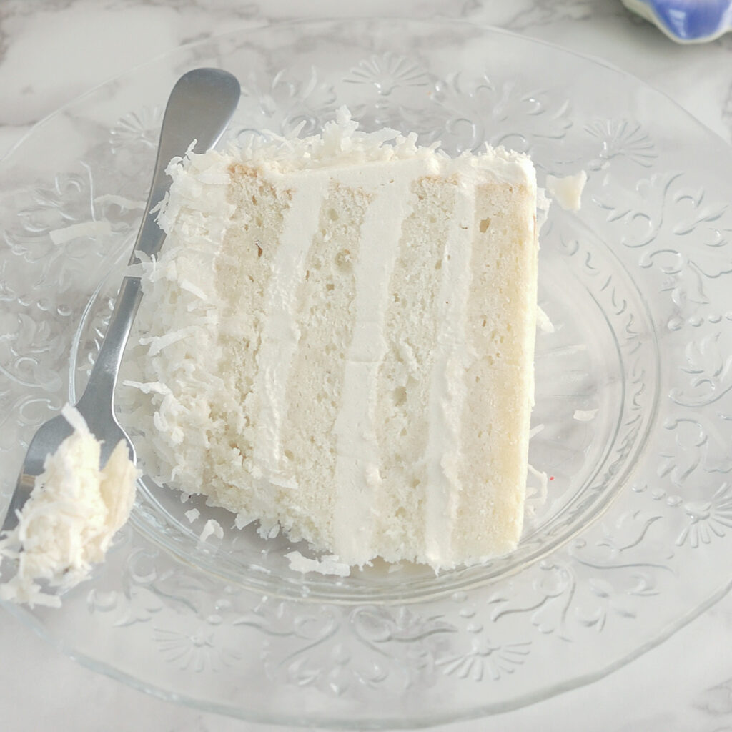 a slice of coconut cake and a fork on a glass plate.