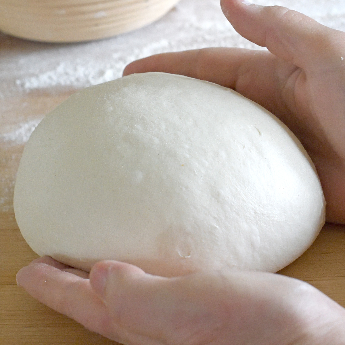 hands forming a ball of bread dough.