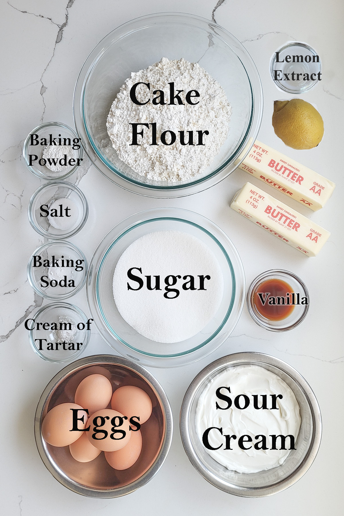 ingredients for lemon cake in glass bowls on a white surface.