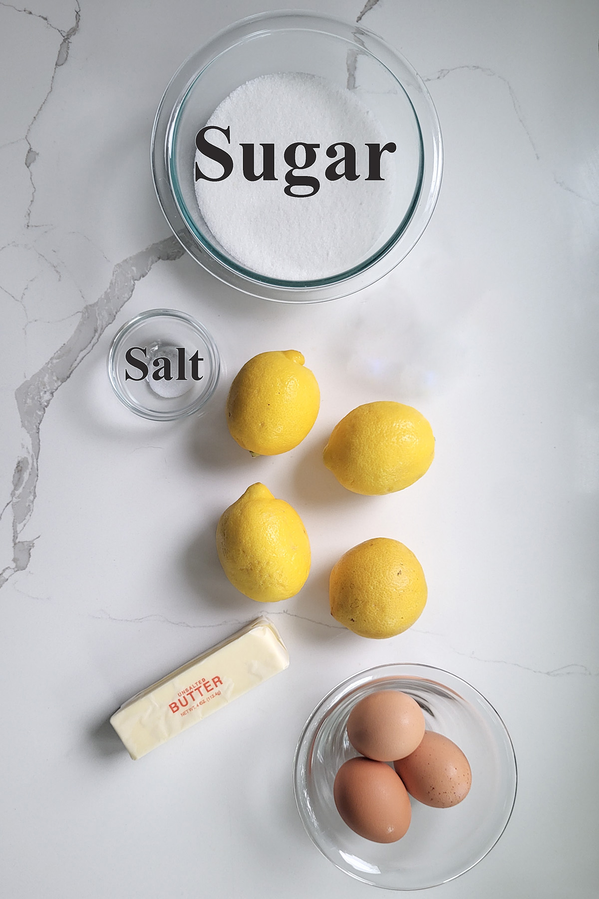 ingredients for lemon curd in glass bowls on white surface.