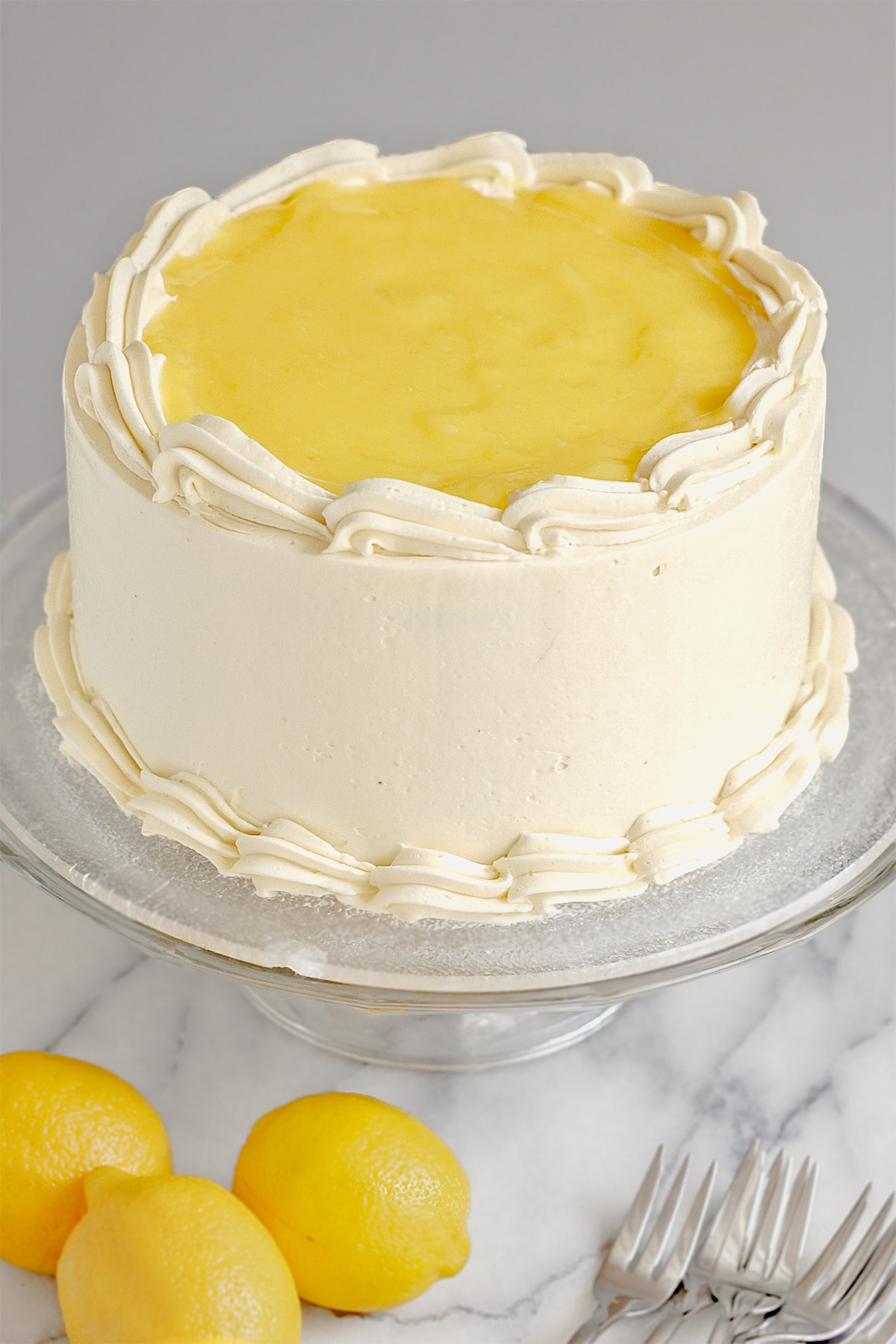 a white iced cake with lemon curd on top on a glass cake stand.