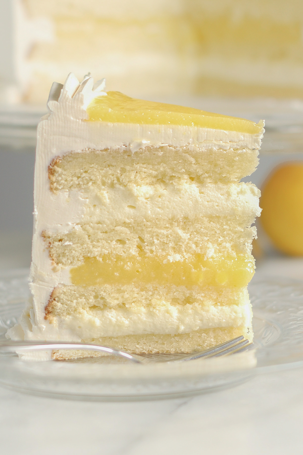 a slice of lemon mousse cake standing on a glass plate.