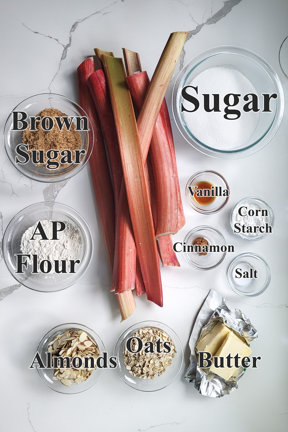 ingredients for rhubarb crisp in glass bowls on a white surface.