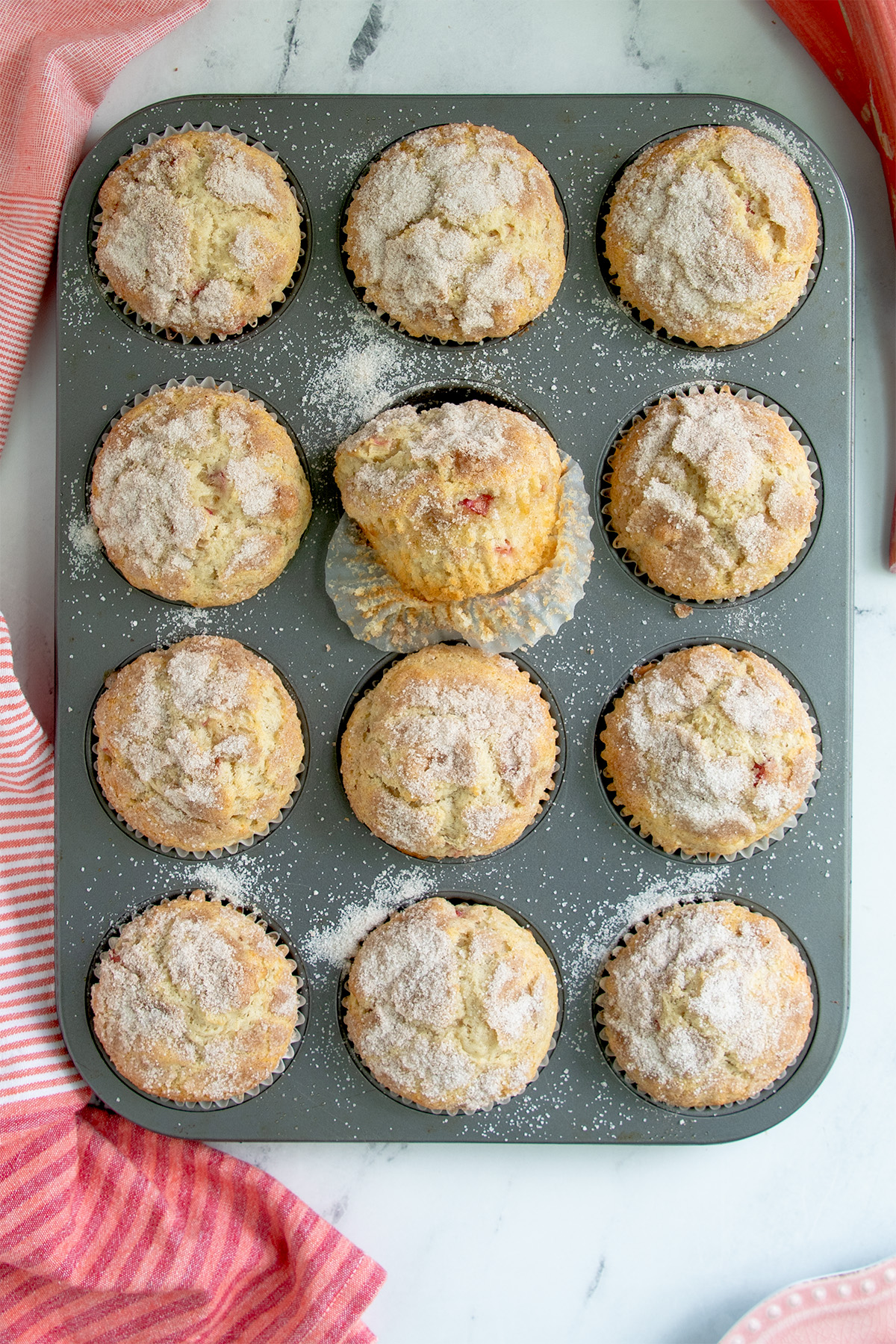 a tray of baked rhubarb muffins on a table with cloth and stalks of rhubarb.