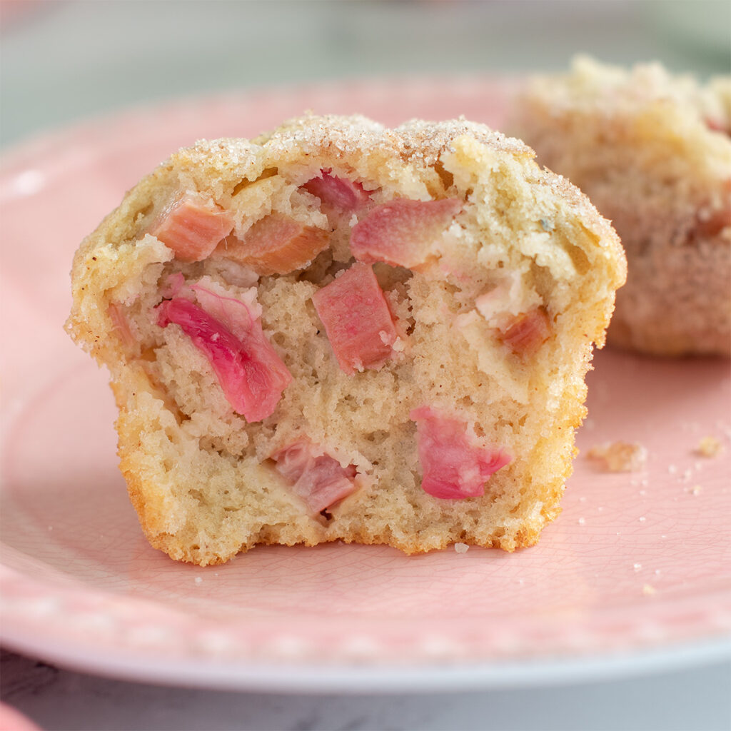 a split rhubarb muffin on a pink plate.