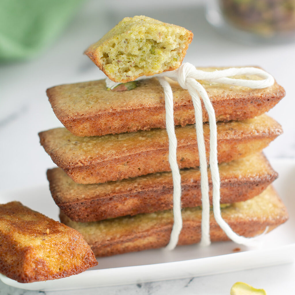 a stack of pistachio financiers on a white plate with kitchen twine tied.