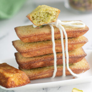 a stack of pistachio financiers on a white plate with kitchen twine tied.