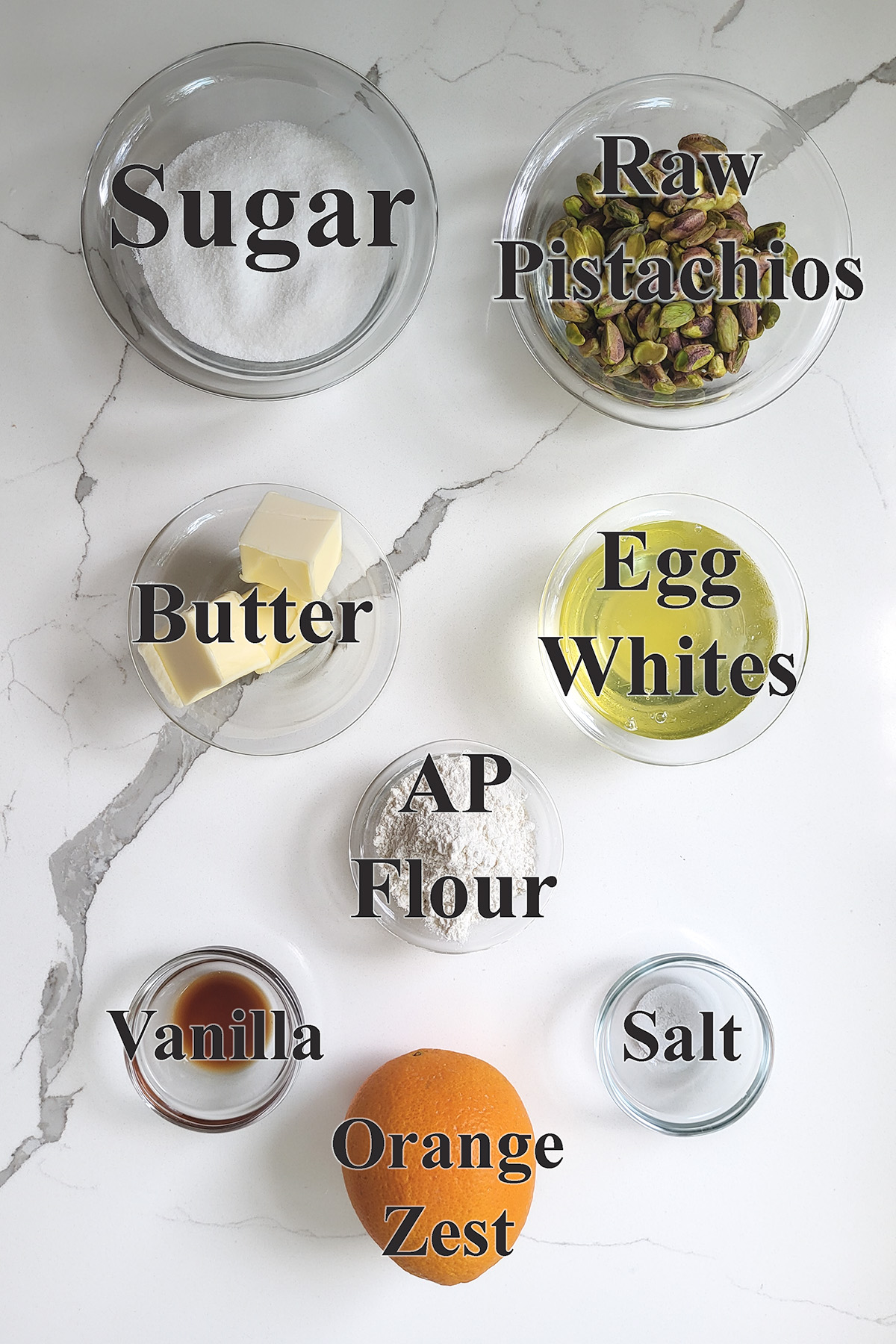 ingredients for pistachio financiers in glass bowls on a white surface.
