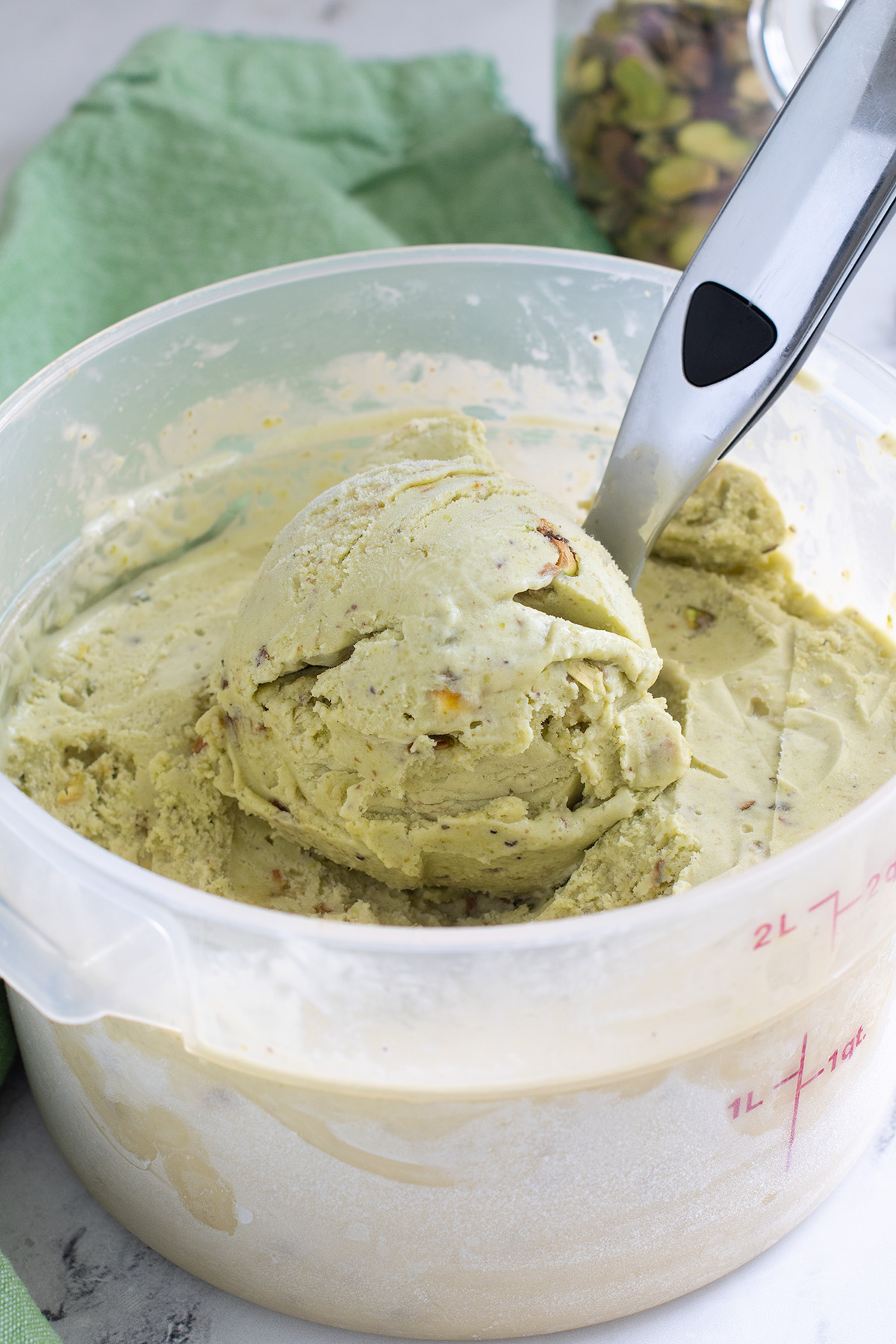 a plastic bin filled with pistachio ice cream with an ice cream scoop.