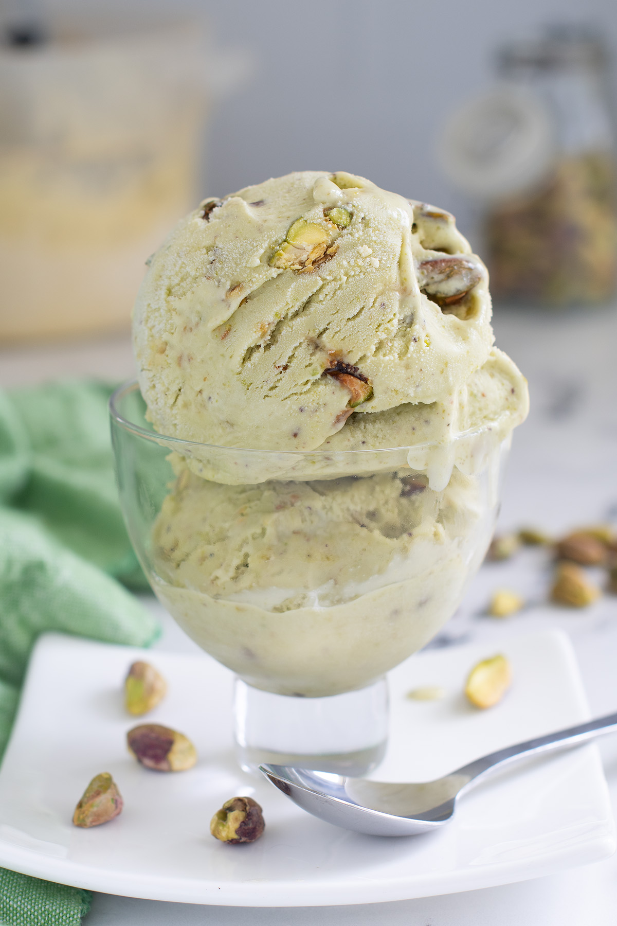 two scoops of pistachio ice cream in a glass bowl on a white plate.