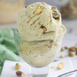 a glass bowl with two scoops of pistachio ice cream on a white plate.