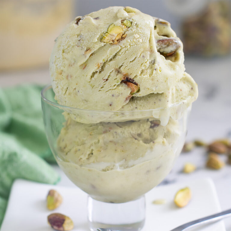 a glass bowl with two scoops of pistachio ice cream on a white plate.