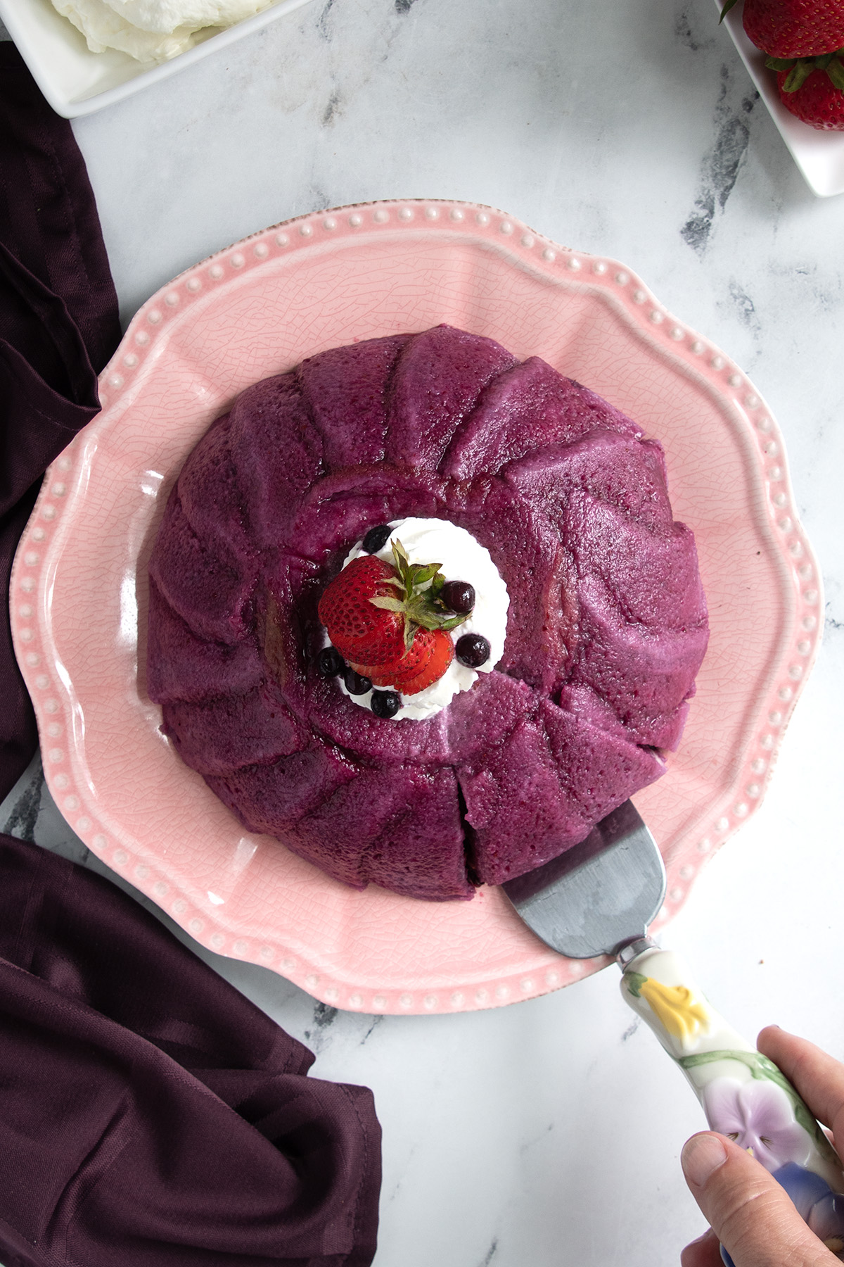 a summer berry pudding on a pink plate with a handing holding a cake server.