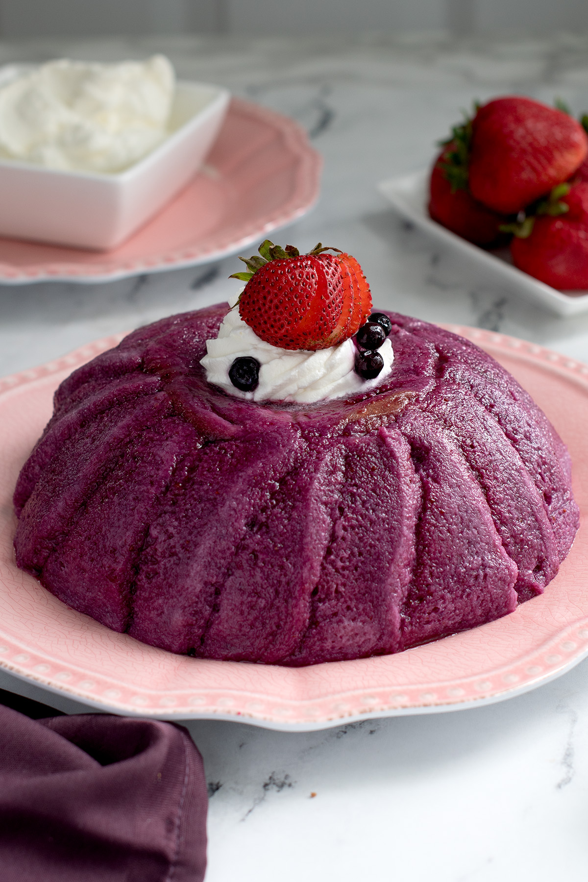a berries pudding with cream on top on a pink plate.