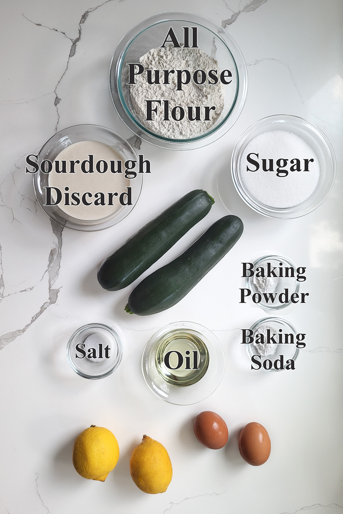 ingredients for sourdough discard zucchini bread in glass bowls on a white surface. 