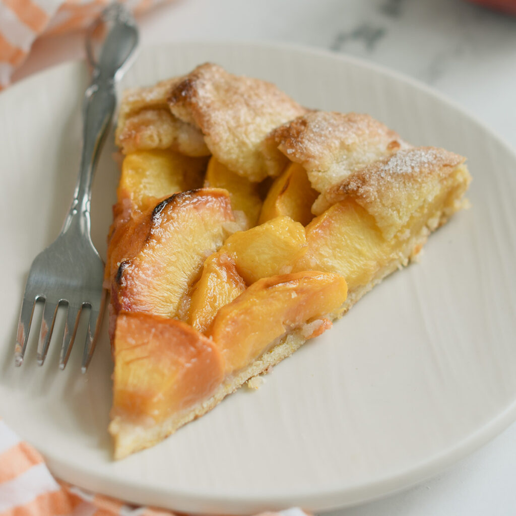 a slice of peach galette on a white plate with a fork.