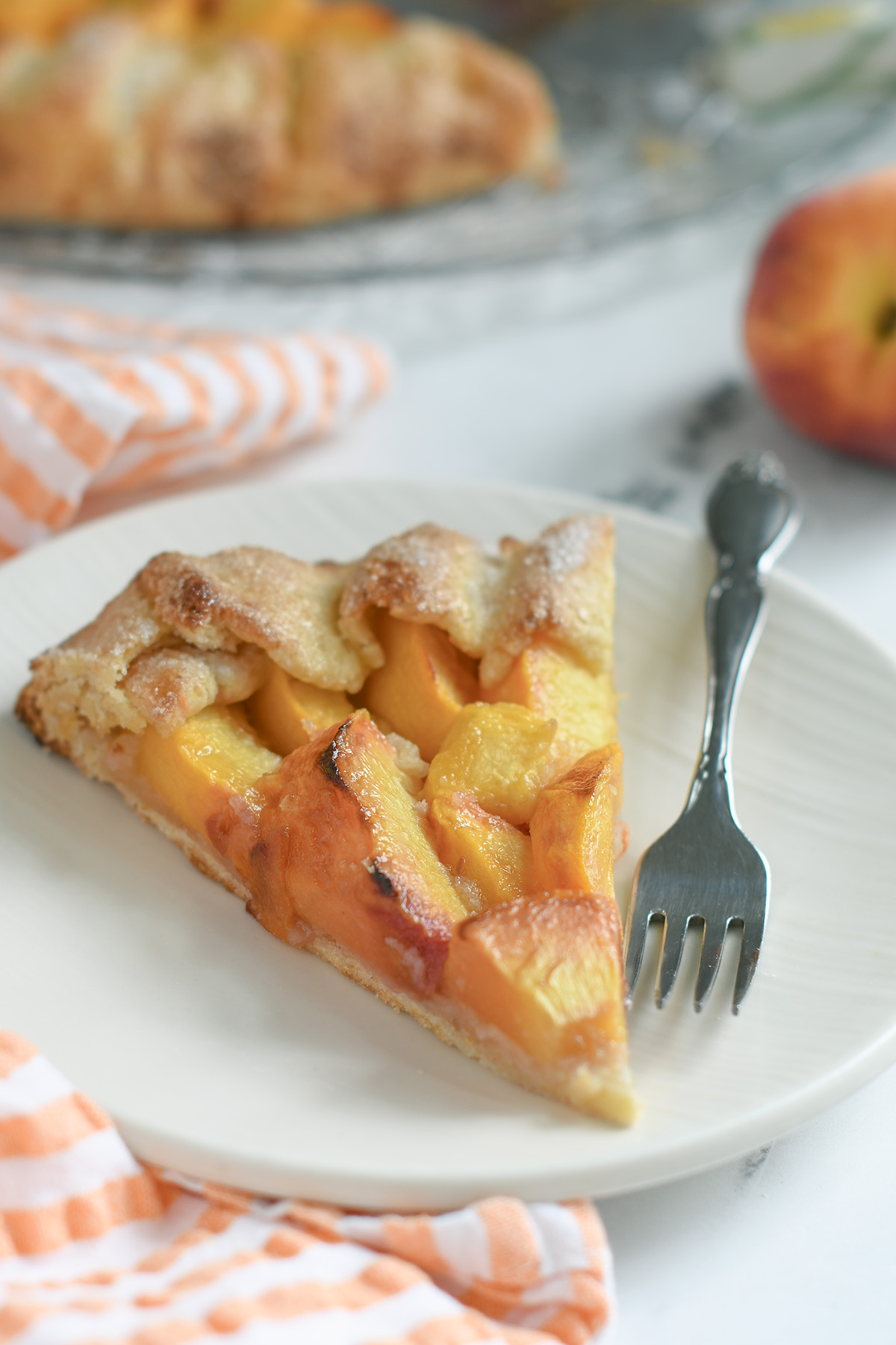 a slice of peach galette in a white plate with a fork.
