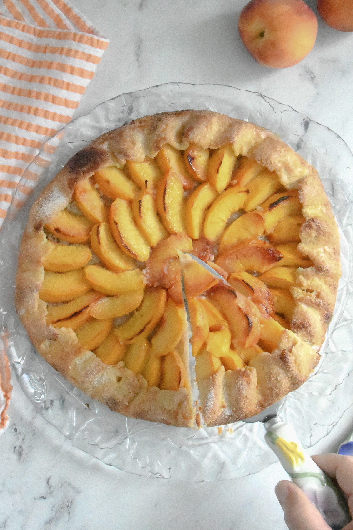 a peach galette on a glass plate with a slice removed.