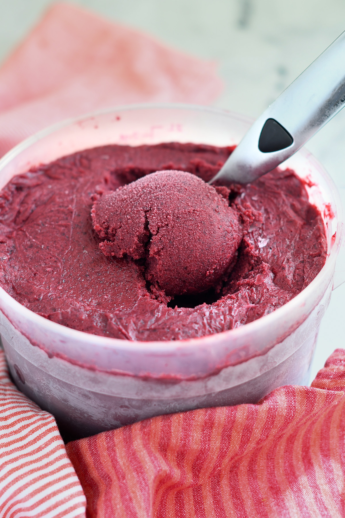 a plastic container filled with cherry sorbet and an ice cream scoop in the sorbet.