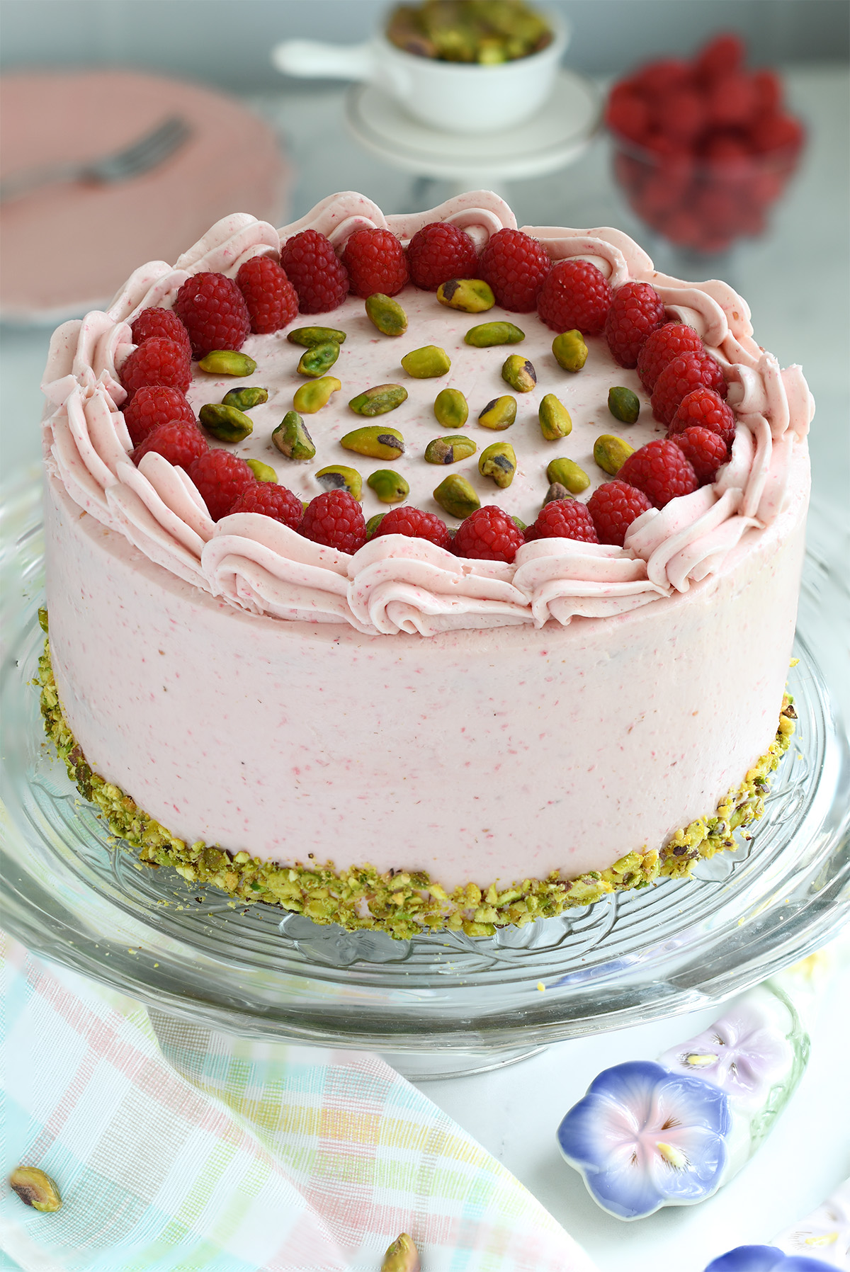 a raspberry and pistachio cake on a glass cake stand. 