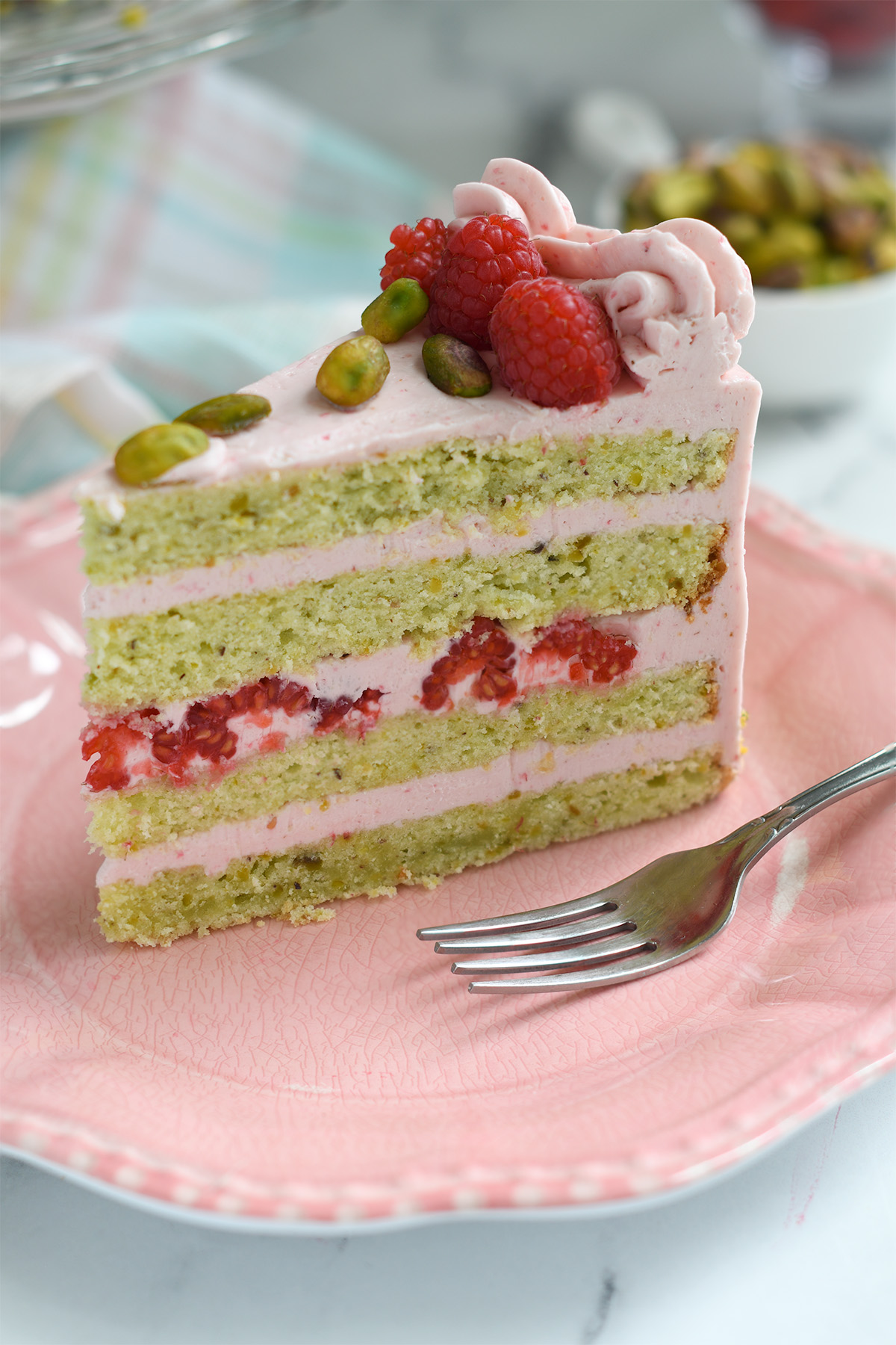 a slice of pistachio raspberry cake on a pink plate.