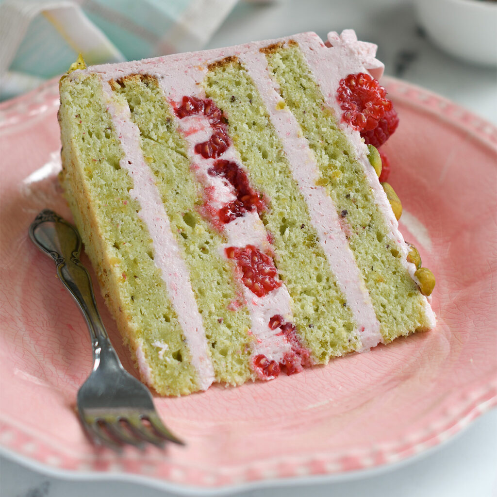 a slice of pistachio raspberry layer cake on a pink plate.