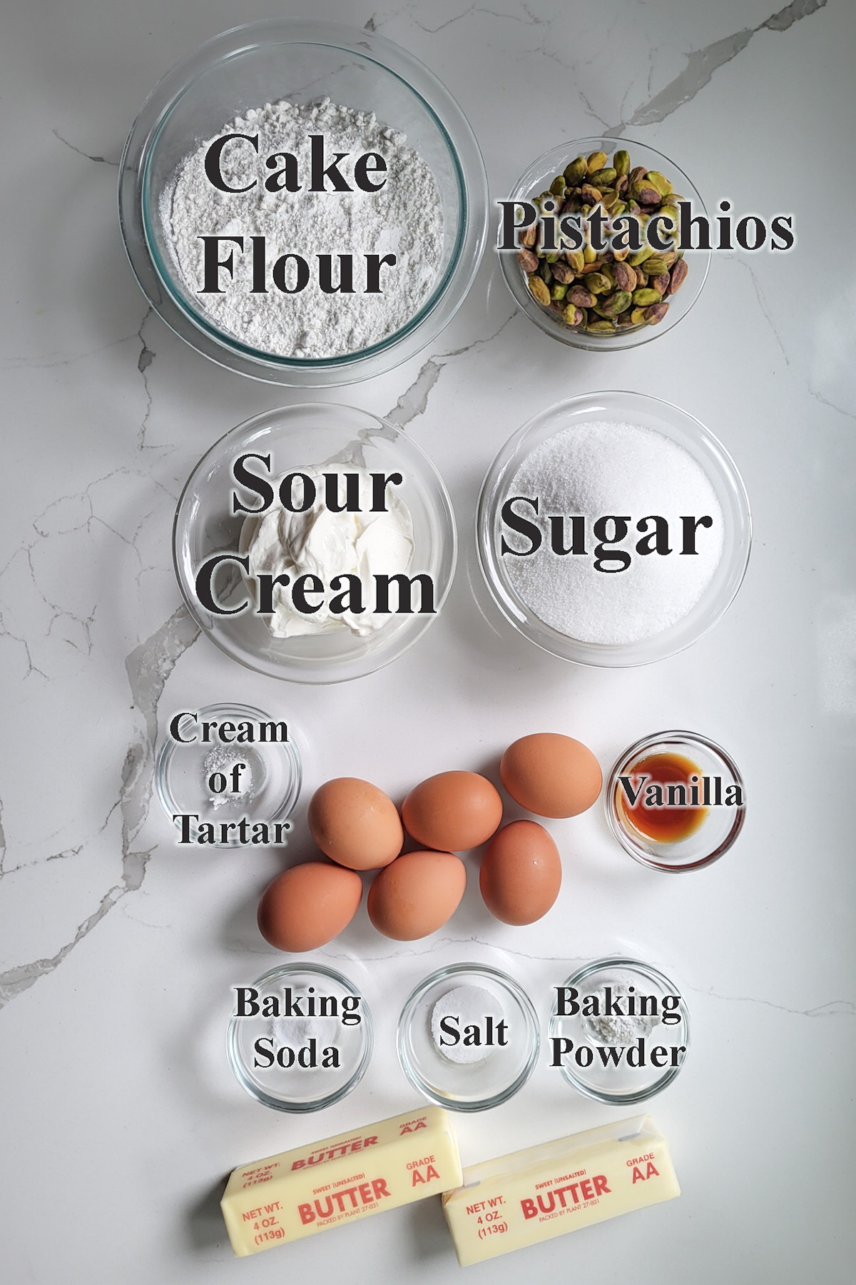 ingredients for pistachio cake in glass bowls on a white surface.