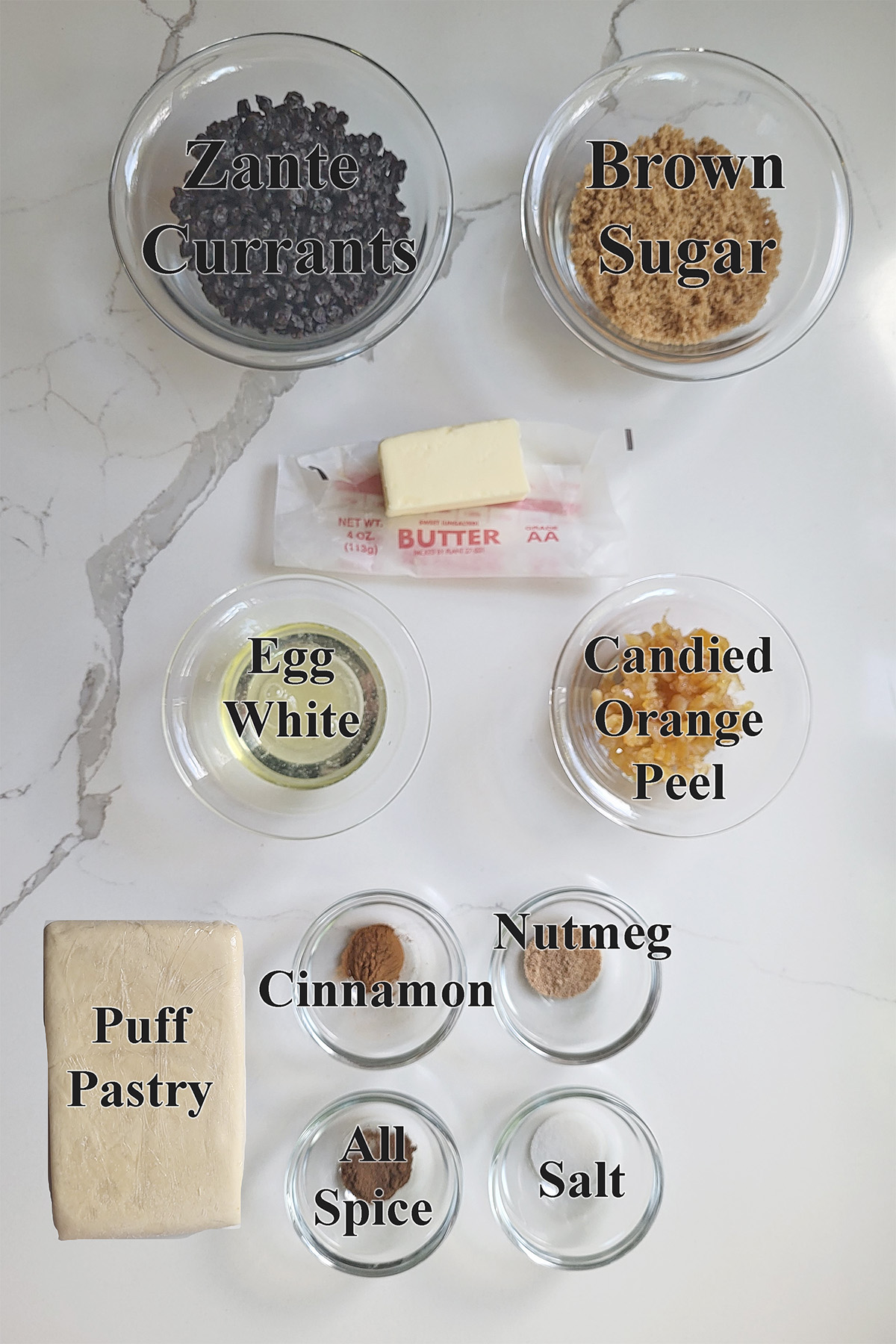 Ingredients for eccles cakes in glass bowls on a white surface.