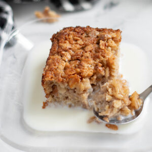 a piece of sourdough baked oatmeal on a plate with milk and a spoon.