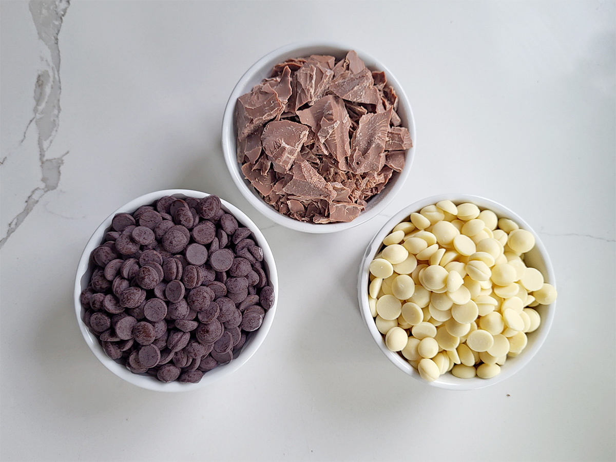 dark, milk and white chocolate in white bowls.