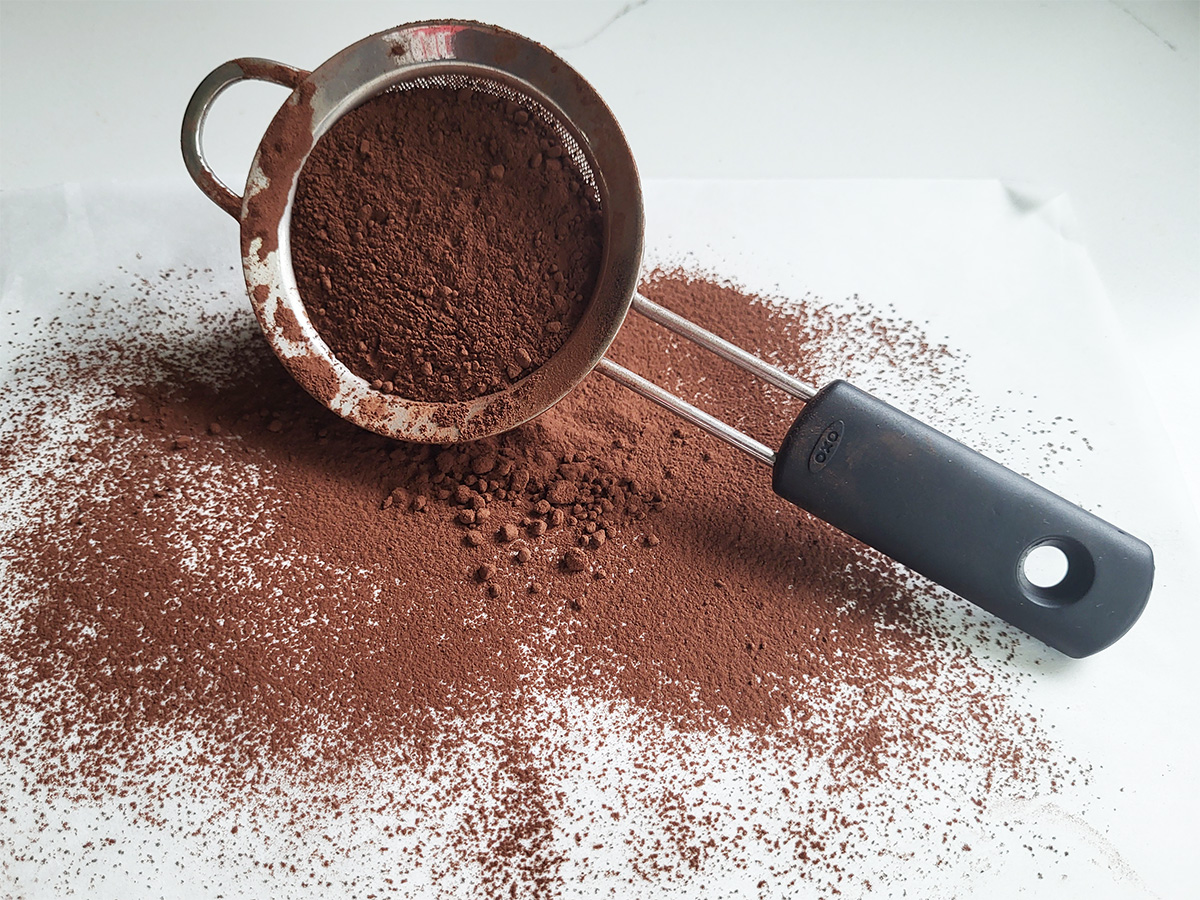 a small sieve filled with cocoa powder spilling on a table.
