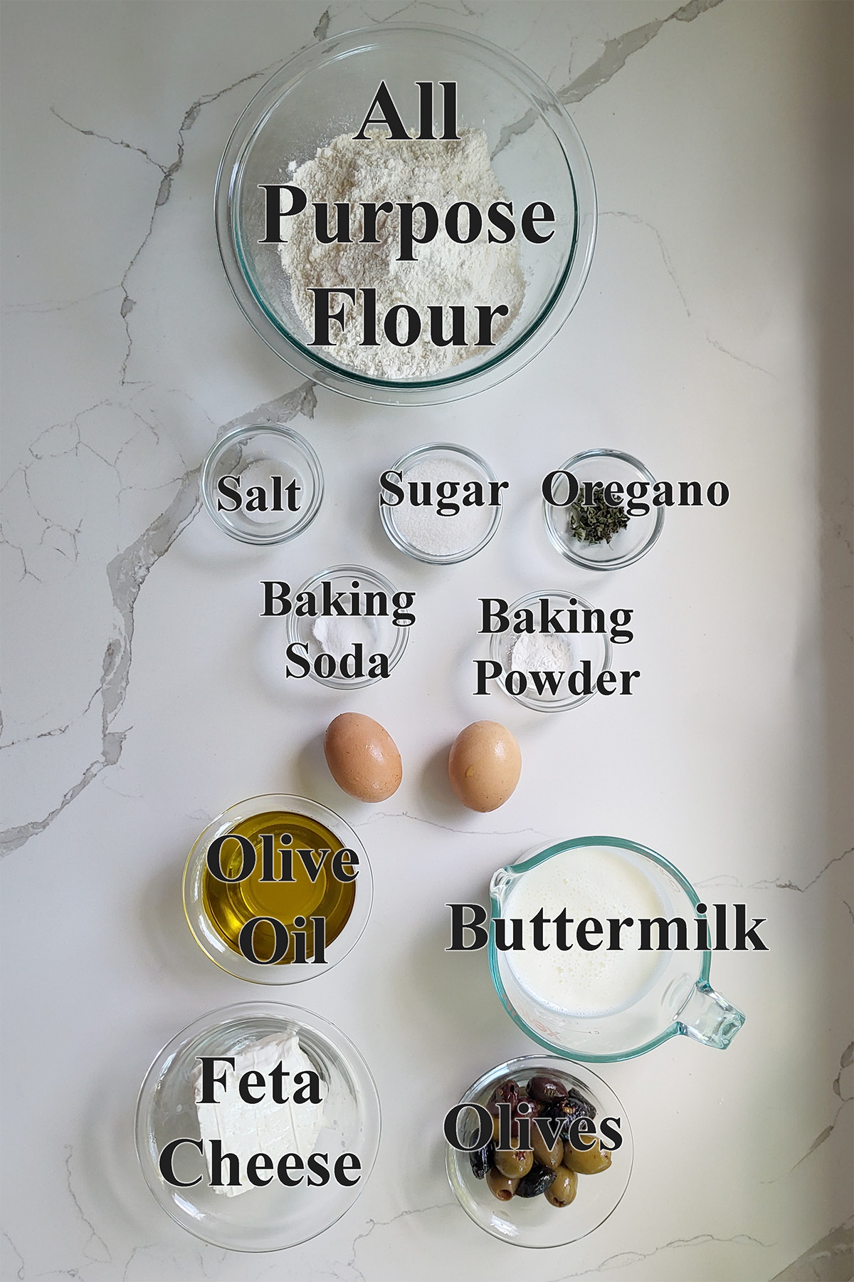 ingredients for savory quick bread in glass bowls on a white surface.