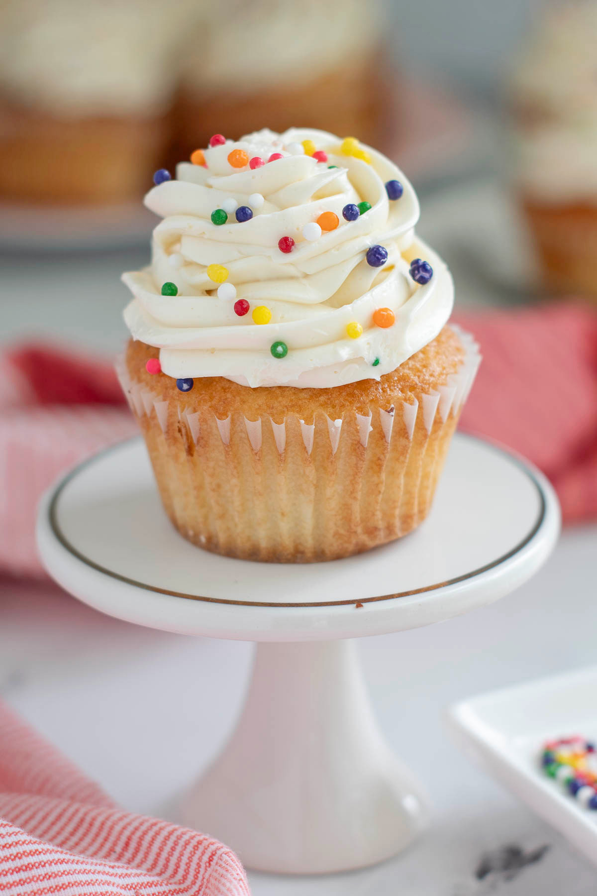 a vanilla cupcake with vanilla frosting and sprinkles on a white plate.