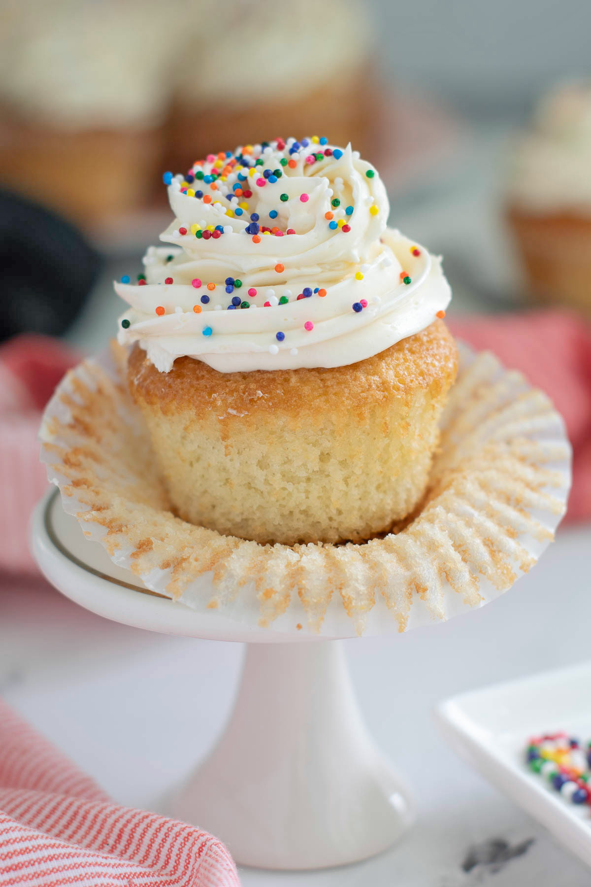 a vanilla cupcake with vanilla frosting and sprinkles on a plate.