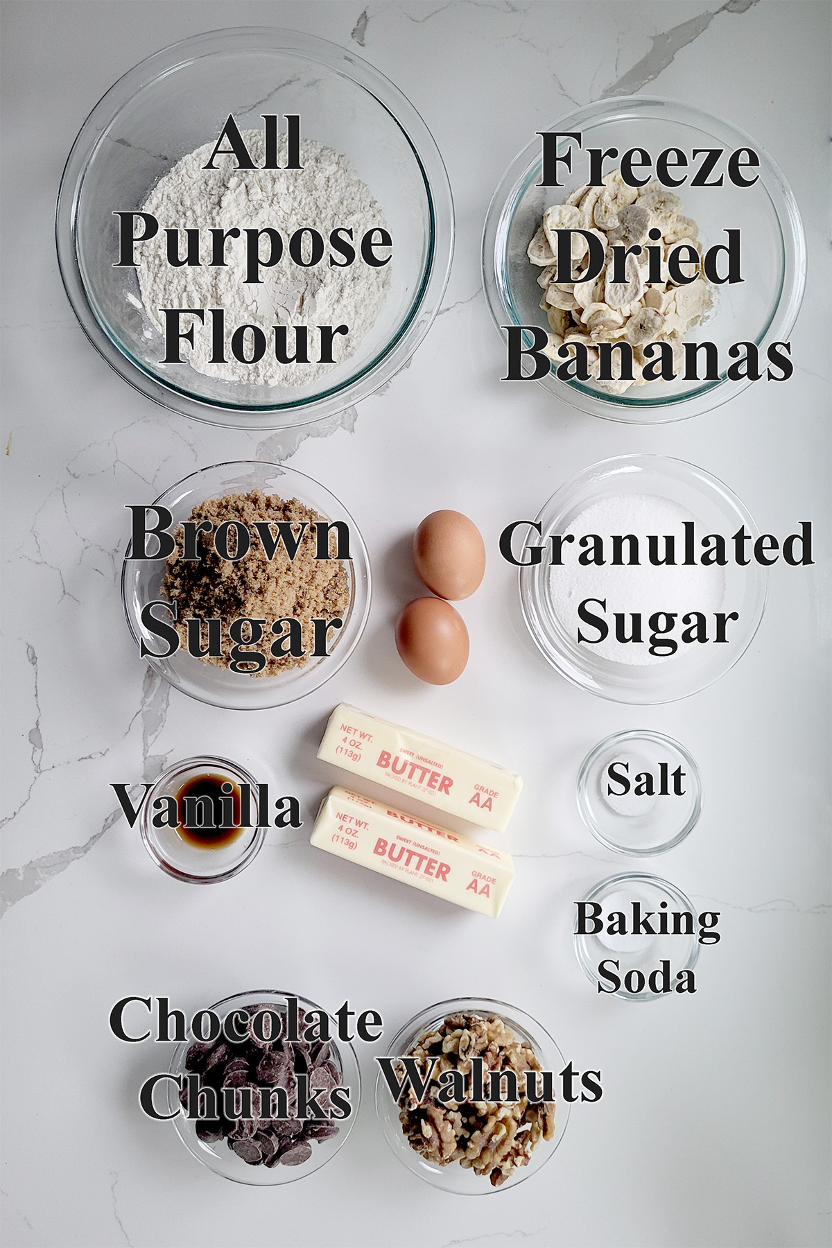 ingredients for banana chocolate chunk cookies in glass bowls on a white surface.
