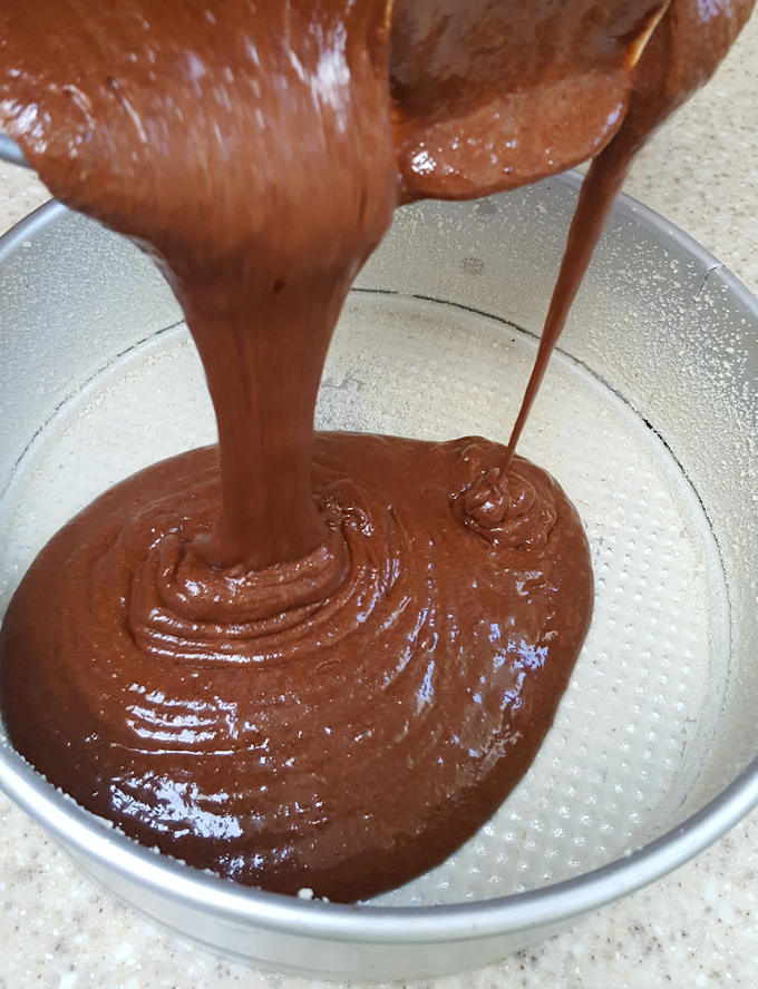 a springform pan buttered and sugared with chocolate cake batter pouring in.
