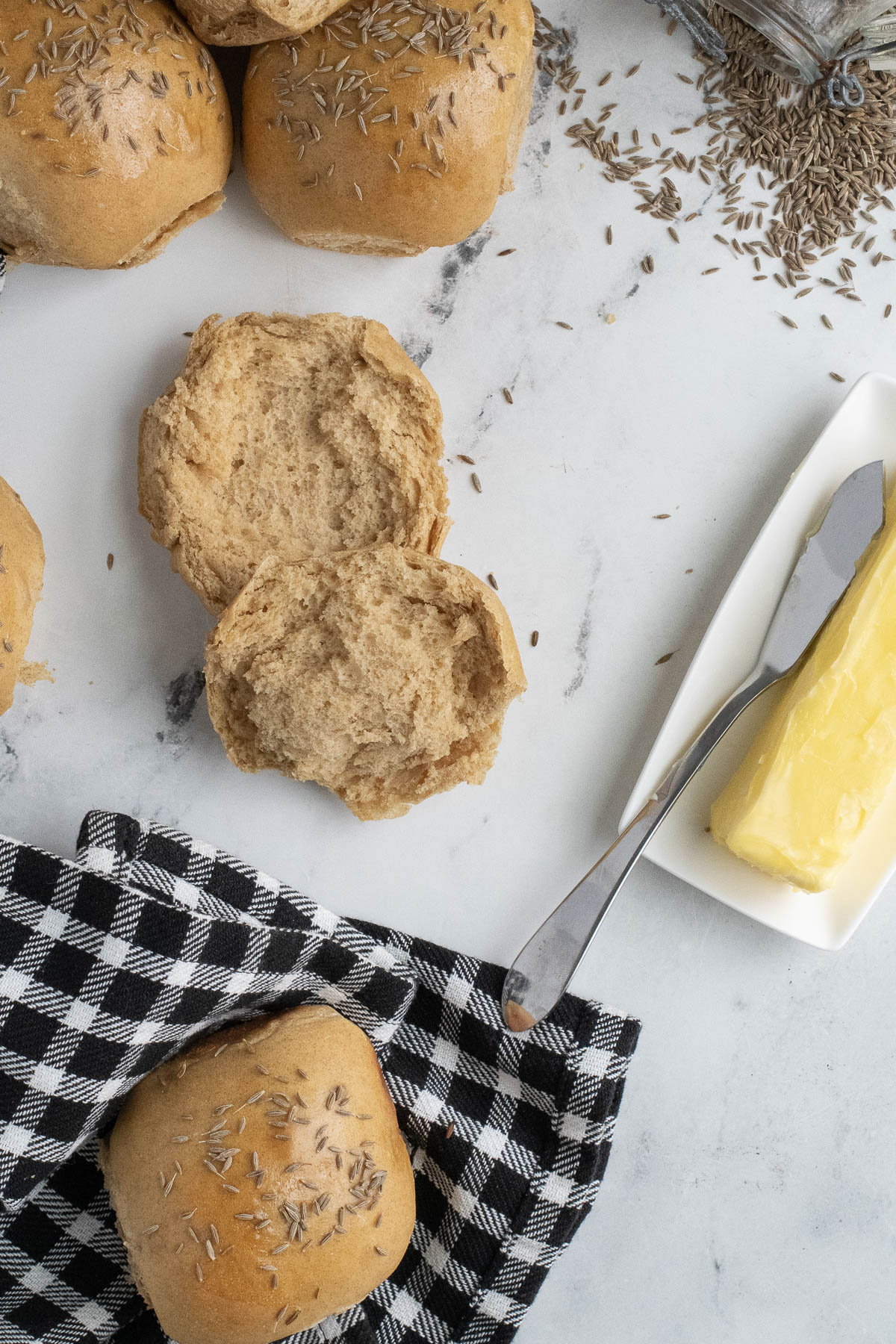 rye dinner rolls on a white surface with a dish of butter.
