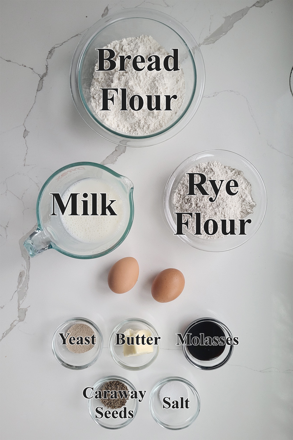 ingredients for rye and molasses dinner rolls in glass bowls on a white surface.