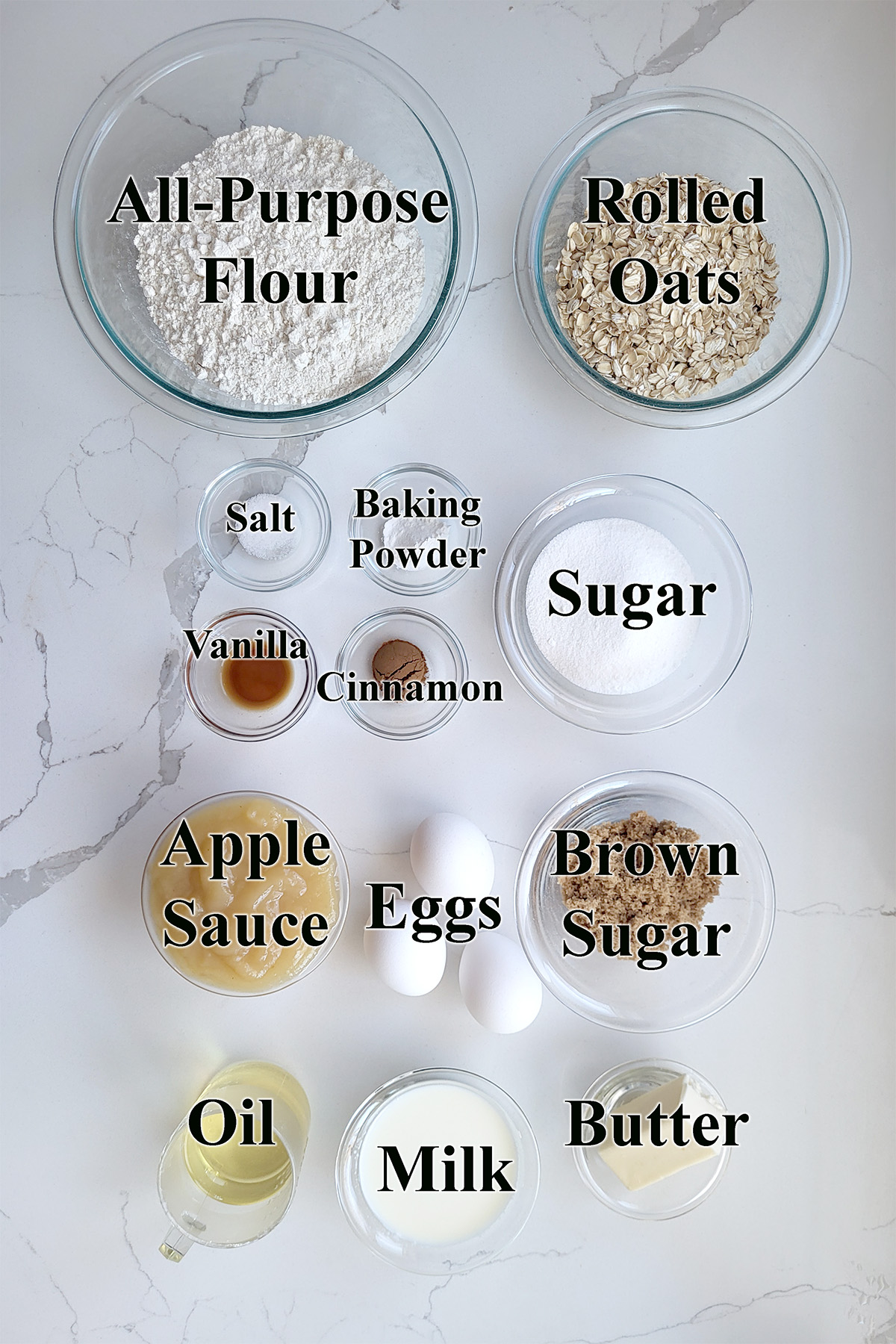 ingredients for applesauce oatmeal muffins in glass bowls on a white surface. 