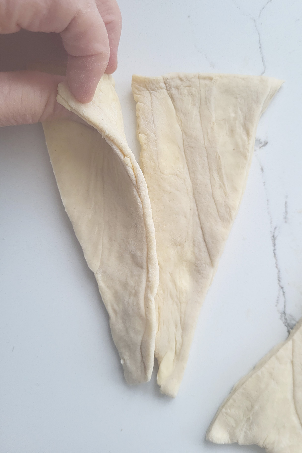 a hand pinching together two triangles of croissant dough.