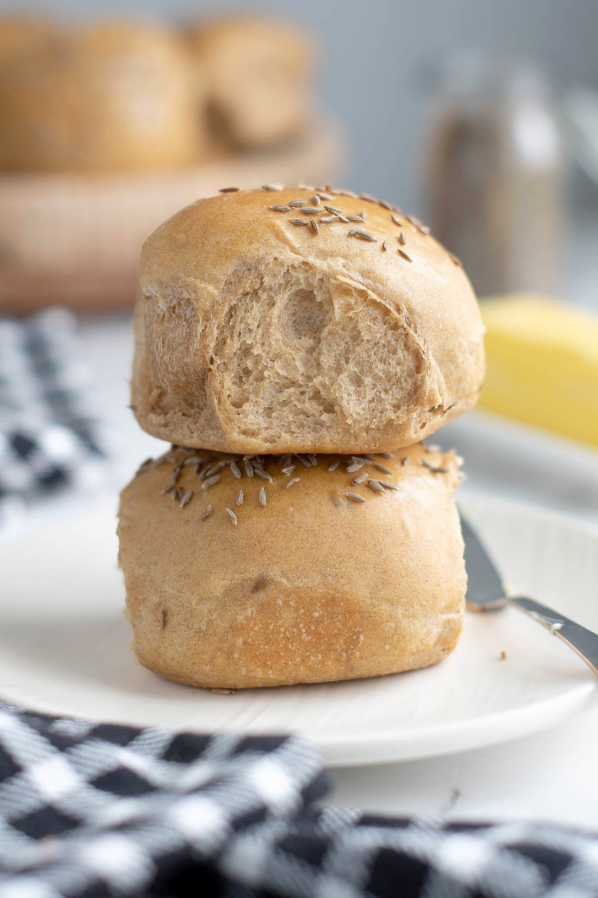 two sourdough rye dinner rolls on a white plate with butter.