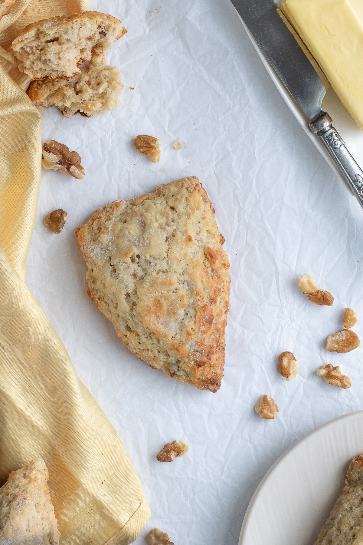 a banana scone, a yellow napkin, walnuts, butter on a parchment paper surface.