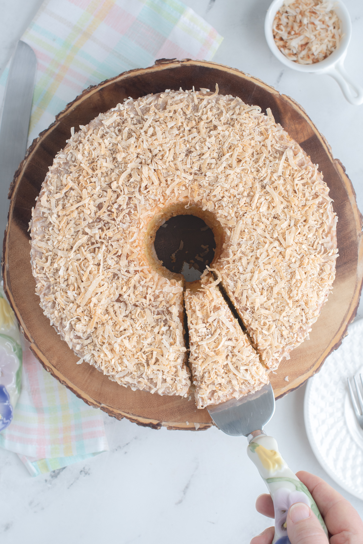 A Coconut chiffon cake on a wooden cake plate with a slice cut. 