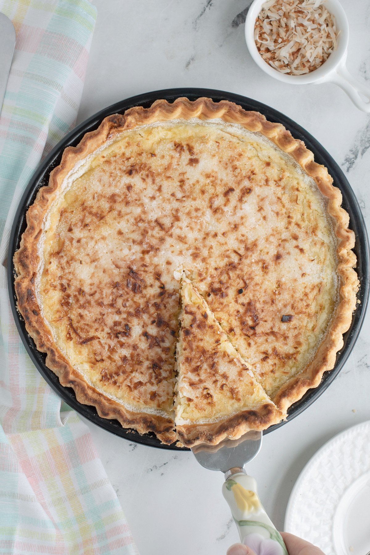 an overhead shot of a coconut custard pie with a slice lifted on cake slicer.