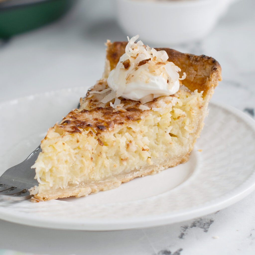a slice of coconut custard pie on a white plate with a fork.