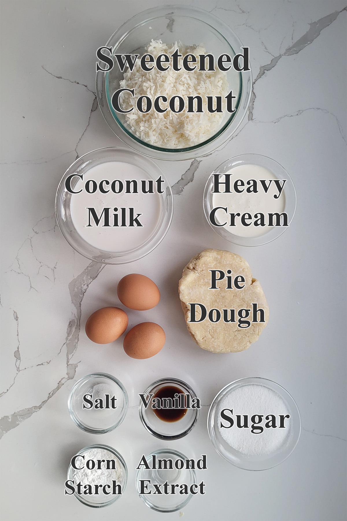 ingredients for coconut custard pie in glass bowls on a white surface.