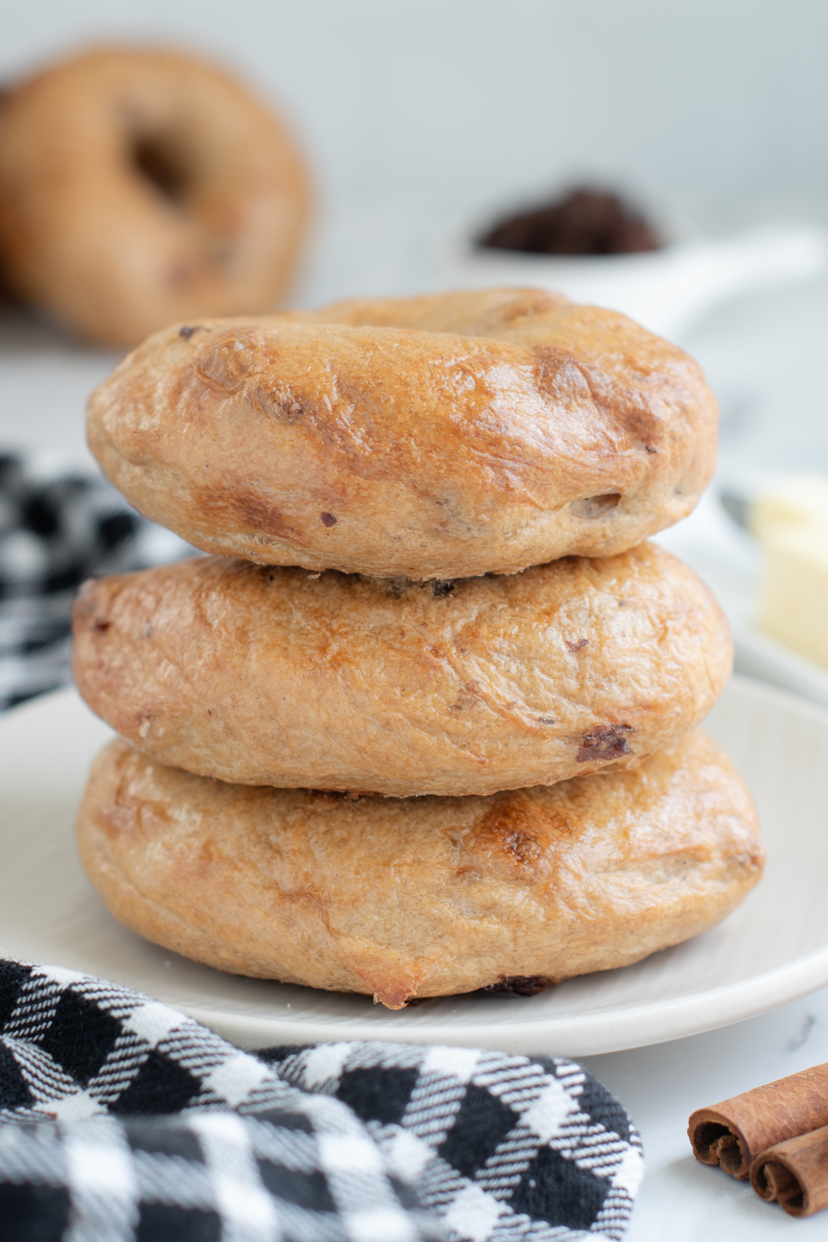 a stack of three sourdough cinnamon raisin bagels on a white plate. 
